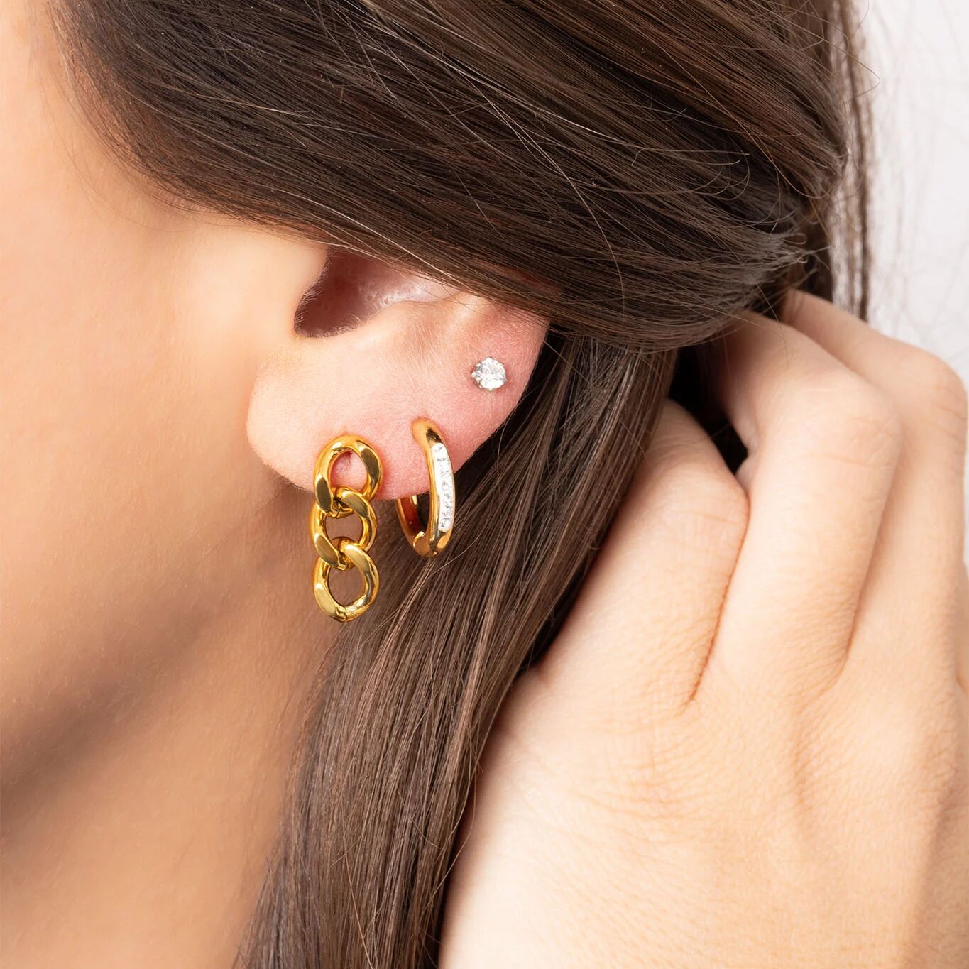 Close-up of a person wearing gold hoop earrings with a neutral background
