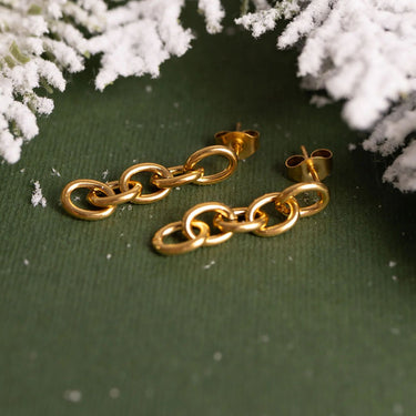 Gold chain earrings on a green surface with snowflake decorations