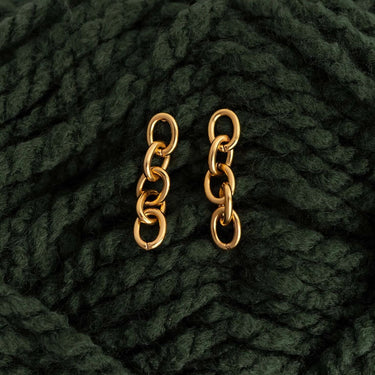 Gold chain earrings on a dark green textured fabric background