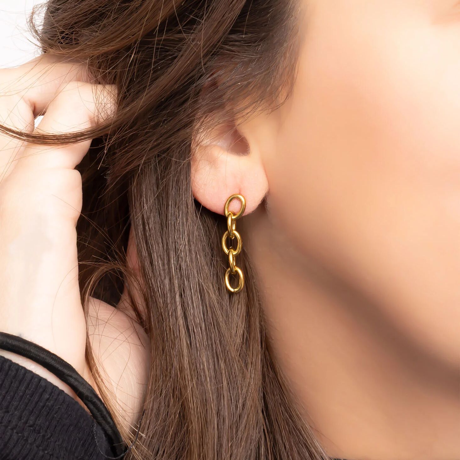 Close-up of a person wearing gold chain earrings with blurred background