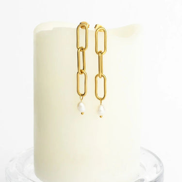 Gold chain earrings with pearl drops on a white candle background