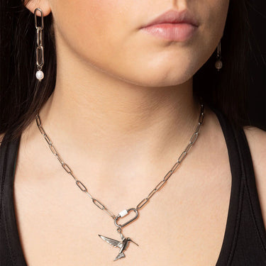 Close-up of a person wearing a necklace with a hummingbird pendant and matching earrings.