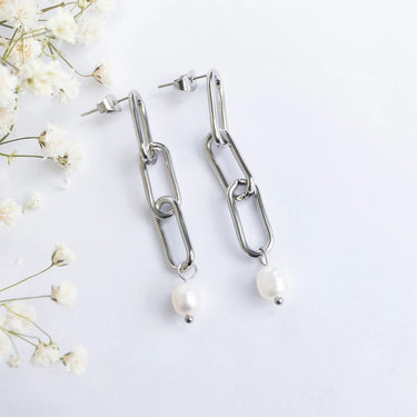 Silver chain earrings with pearl drops on a light background with flowers.