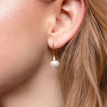 Close-up of an ear wearing a gold earring with a pearl drop.
