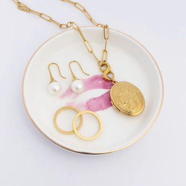 Gold necklace with a lock-shaped pendant, pearl earrings, and gold rings on a white dish with floral design.