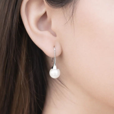 Pearl earring worn by a person with dark hair, close-up of ear.