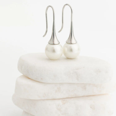 Pearl earrings on a marble surface with a white background