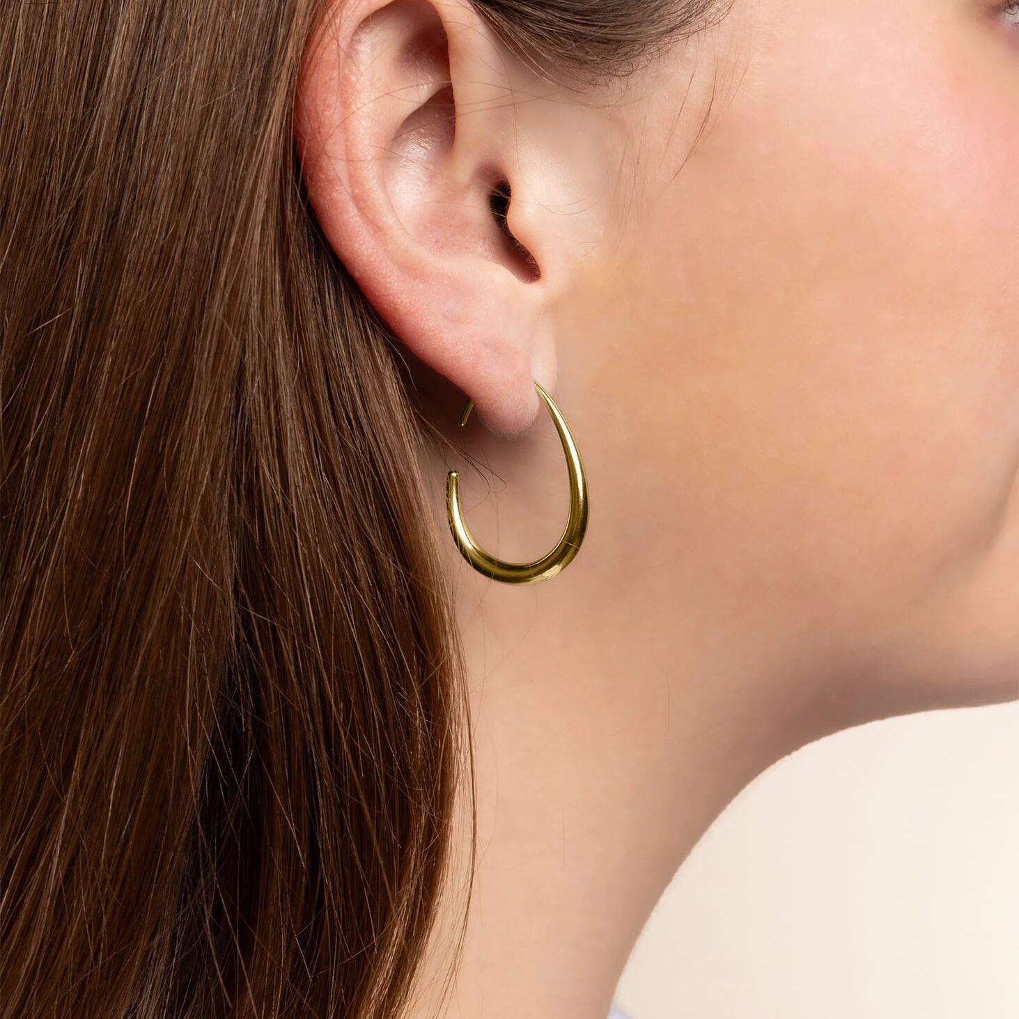Close-up of a person wearing a gold hoop earring with a neutral background