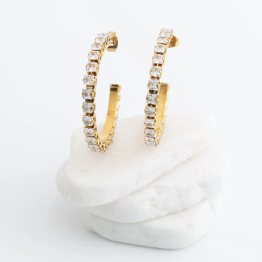 Gold hoop earrings with clear stones on a white marble surface