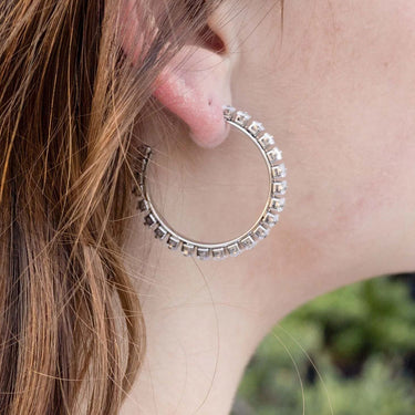Close-up of a person wearing a silver hoop earring with small stones.