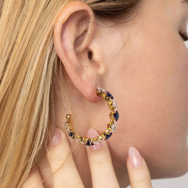 Gold hoop earring with embedded stones worn by a person