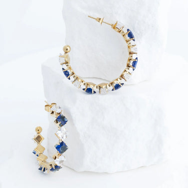 Gold hoop earrings with blue and clear gemstones on a white background