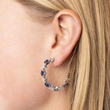 Close-up of an ear wearing a hoop earring with blue and clear stones.