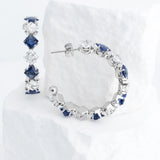 Pair of silver hoop earrings with blue gemstones on a white background
