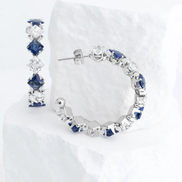 Pair of silver hoop earrings with blue gemstones on a white background