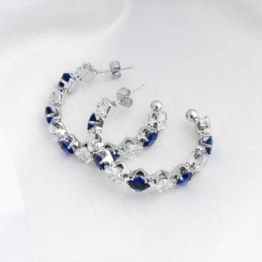 Pair of silver hoop earrings with blue gemstones on a white silk background