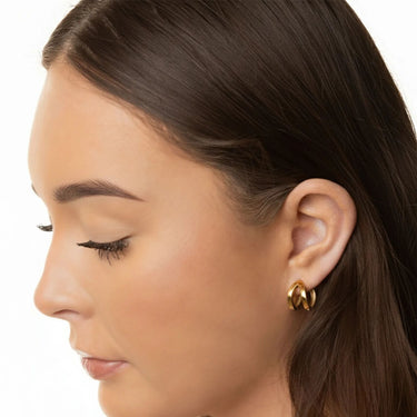 Close-up of a woman wearing gold hoop earrings on a white background