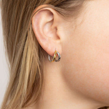 Close-up of an ear wearing gold and silver hoop earrings with blonde hair.