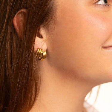 Close-up of a person wearing gold hoop earrings with a blurred background