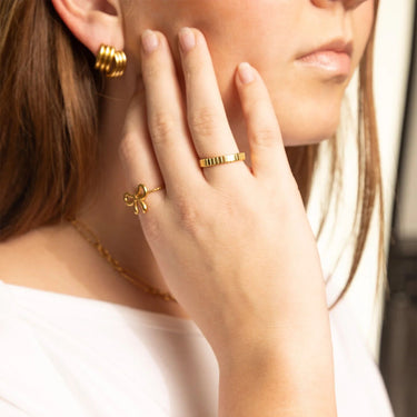 Close-up of a woman wearing gold jewelry including earrings, a ring, and a necklace.