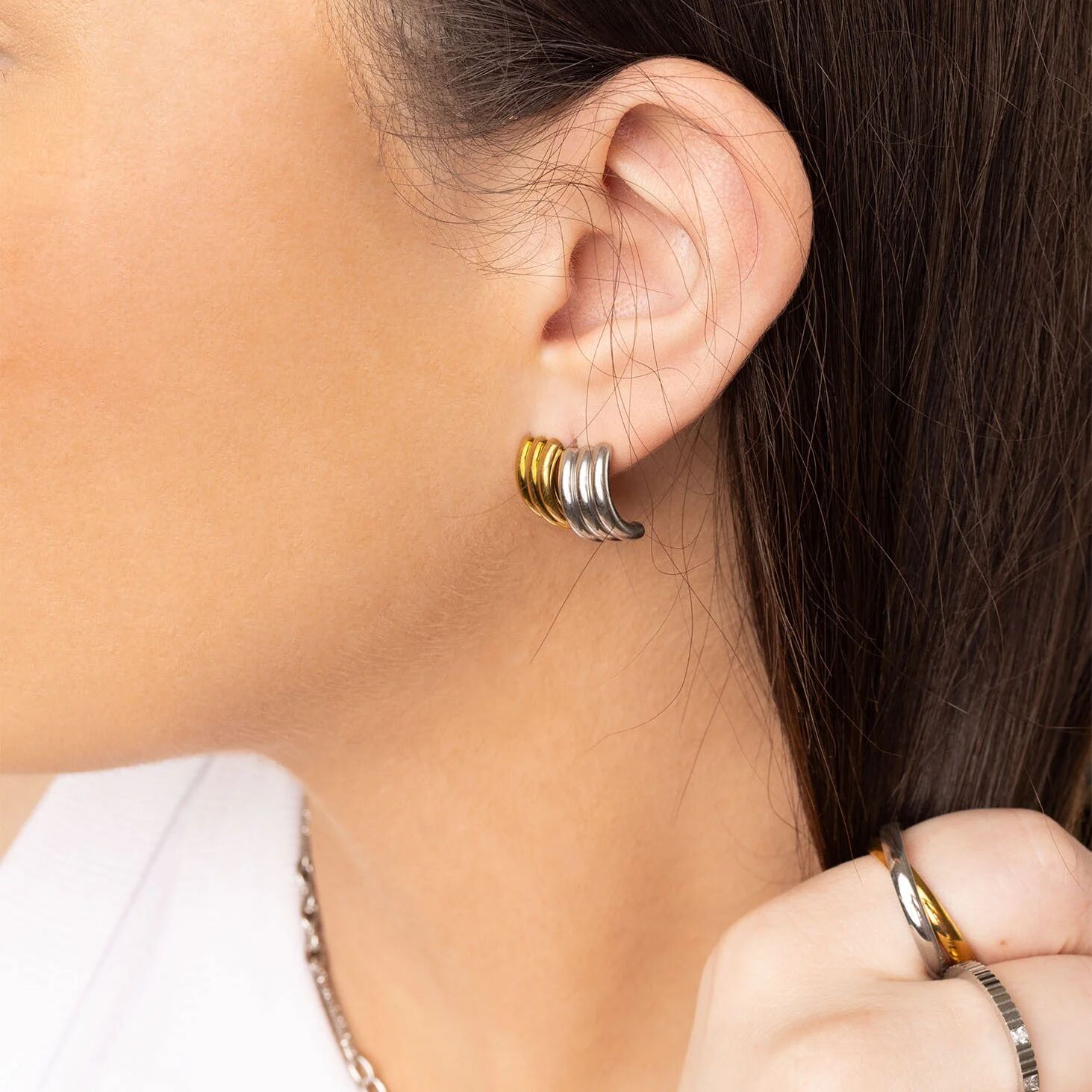 Close-up of an ear wearing a set of hoop earrings with a hand holding a ring.