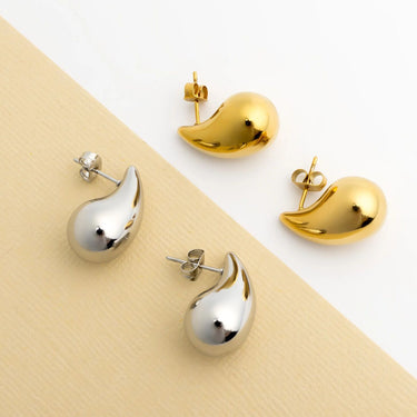 Gold and silver teardrop-shaped earrings on a beige and white background