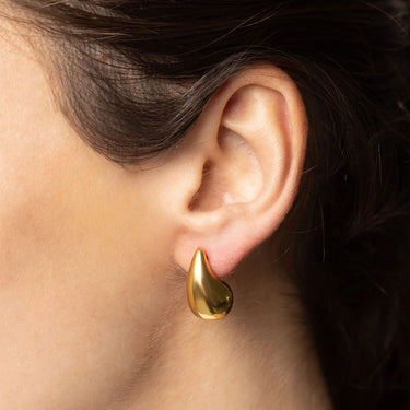 Gold teardrop earring worn on an ear with dark hair.
