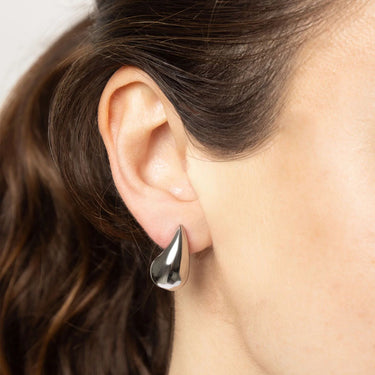 Silver teardrop earring worn by a person with dark hair.
