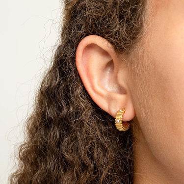 Close-up of an ear wearing a gold hoop Fluted Huggie with Stones Earrings with a plain background