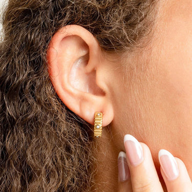 Close-up of a person wearing a gold hoop Fluted Huggie with Stones Earrings with a blurred background