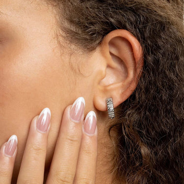 Close-up of an ear wearing a silver Fluted Huggie with Stones Earrings with a hand touching the cheek.