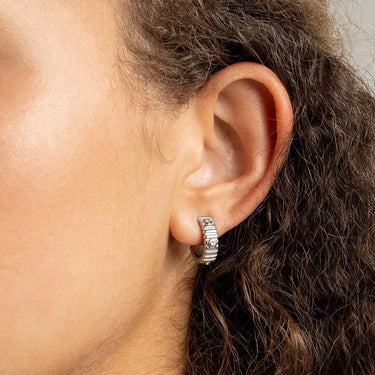 Close-up of an ear wearing a silver hoop Fluted Huggie with Stones Earrings with hair partially covering the frame.
