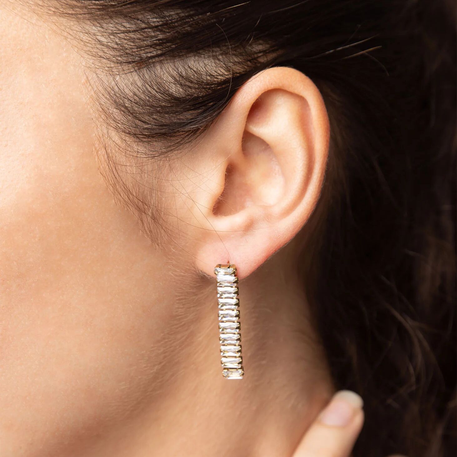 Close-up of an ear wearing a gold hoop earring with clear stones.