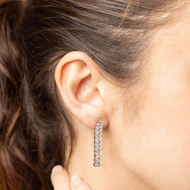 Close-up of an ear wearing a diamond hoop earring with hair partially obscuring the view.