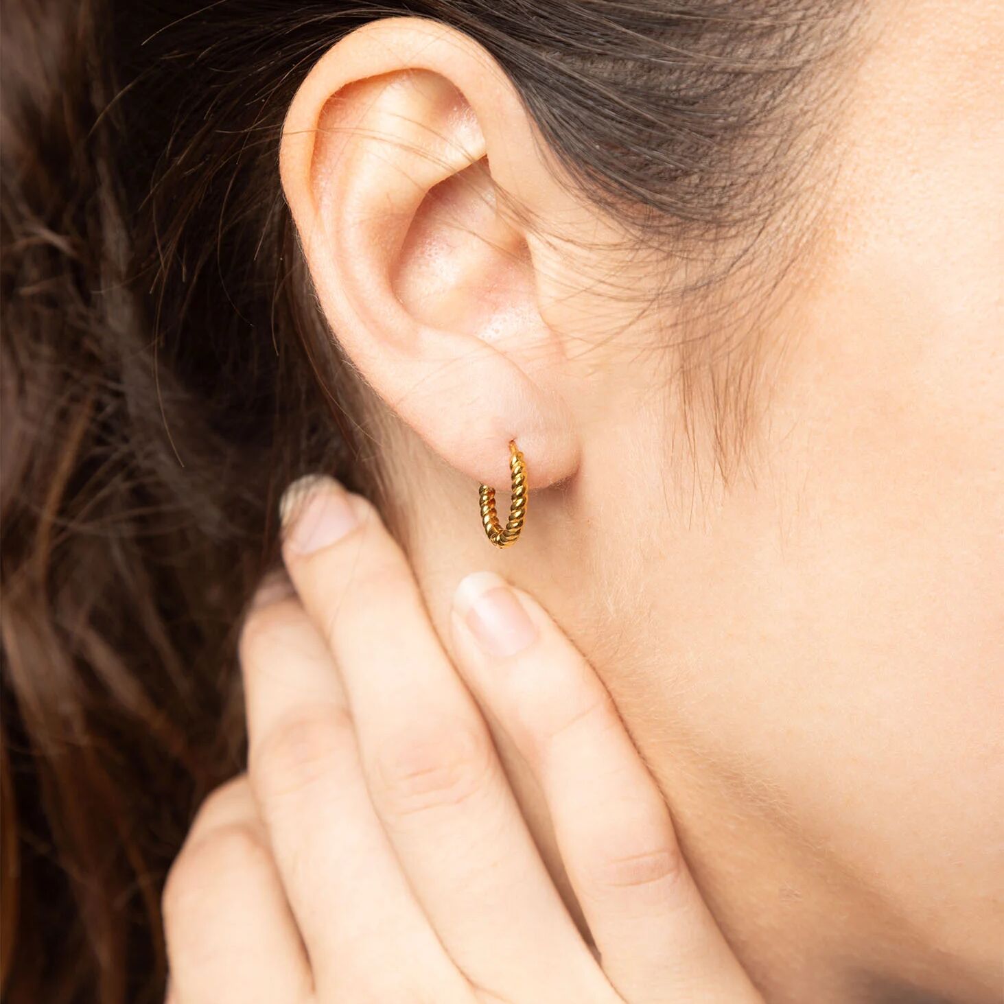Close-up of a person wearing gold hoop earrings with a blurred background