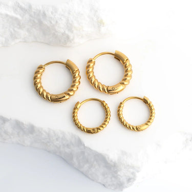 Set of gold hoop earrings on a white marble surface