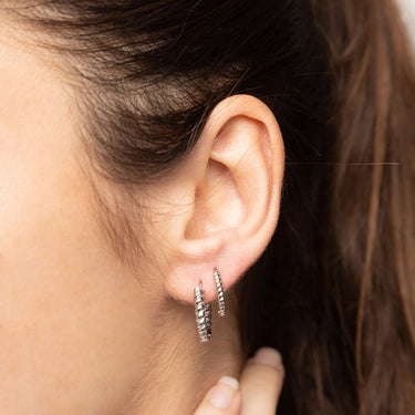 Close-up of an ear wearing two silver hoop earrings with a blurred background