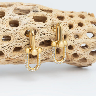 Gold earrings with small pearls on a textured beige surface