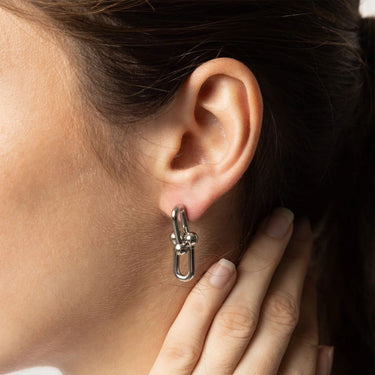 Close-up of an ear wearing a silver earring with a hand touching the earlobe.