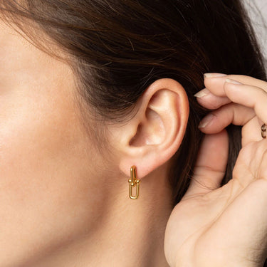 Gold earring worn by a person with a close-up of the ear and hand.