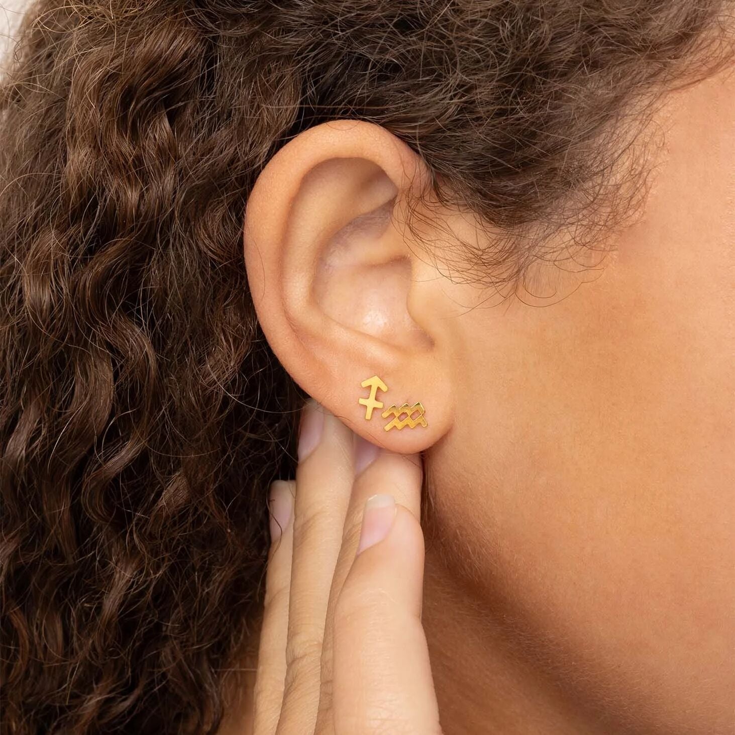 Gold 'Fame' earring on a person's ear with a blurred background