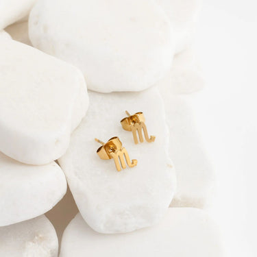 Gold letter 'm' earrings on a white stone background