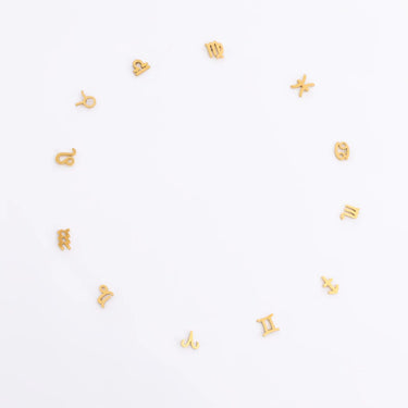 Gold zodiac charm pieces scattered on a white background