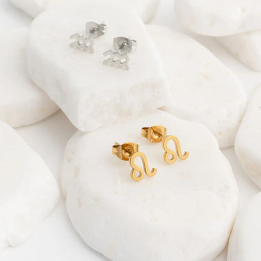 Gold and silver letter zodiac earrings on a white stone background