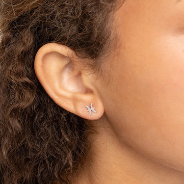 Close-up of an ear wearing a star-shaped earring with hair partially obscuring the view.