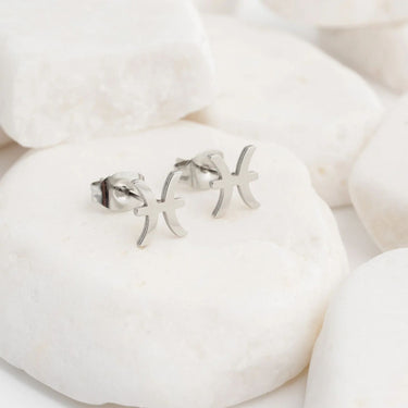 Silver letter zodiac earrings on a white stone background