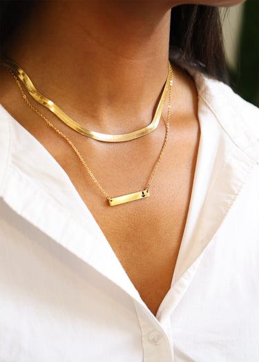 Gold necklace with a bar pendant on a person wearing a white shirt.