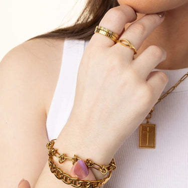Hand wearing gold jewelry with a cross pendant on a white background