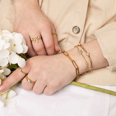 Close-up of hands wearing gold jewelry with a beige jacket and white flowers.