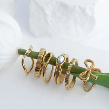 Set of gold rings with various designs on a green stick against a white background
